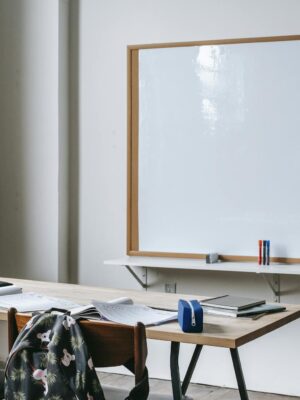 An empty classroom with wooden desks, chairs, and a large whiteboard for teaching.